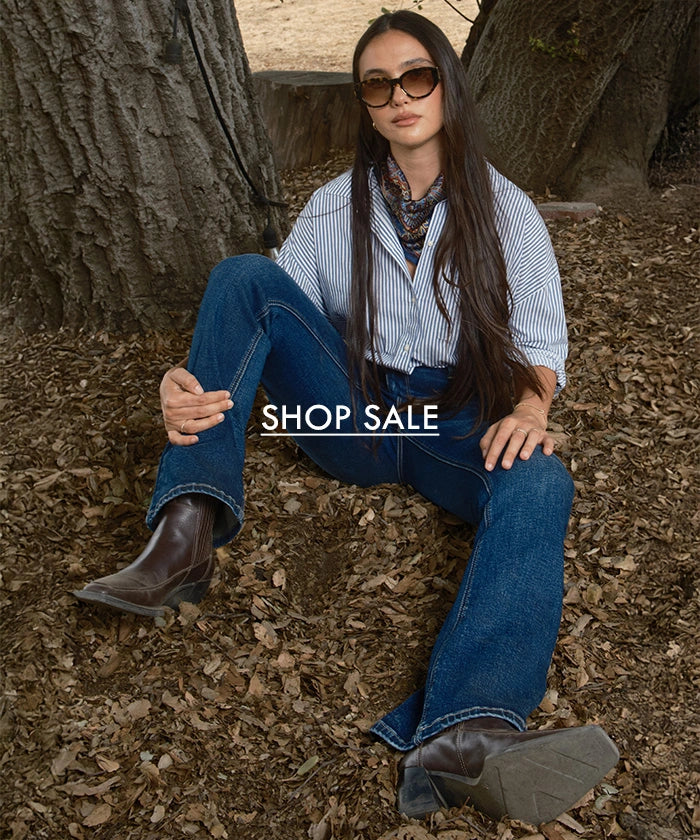 Woman sitting on the ground with text overlay 'SHOP SALE' in a natural setting.