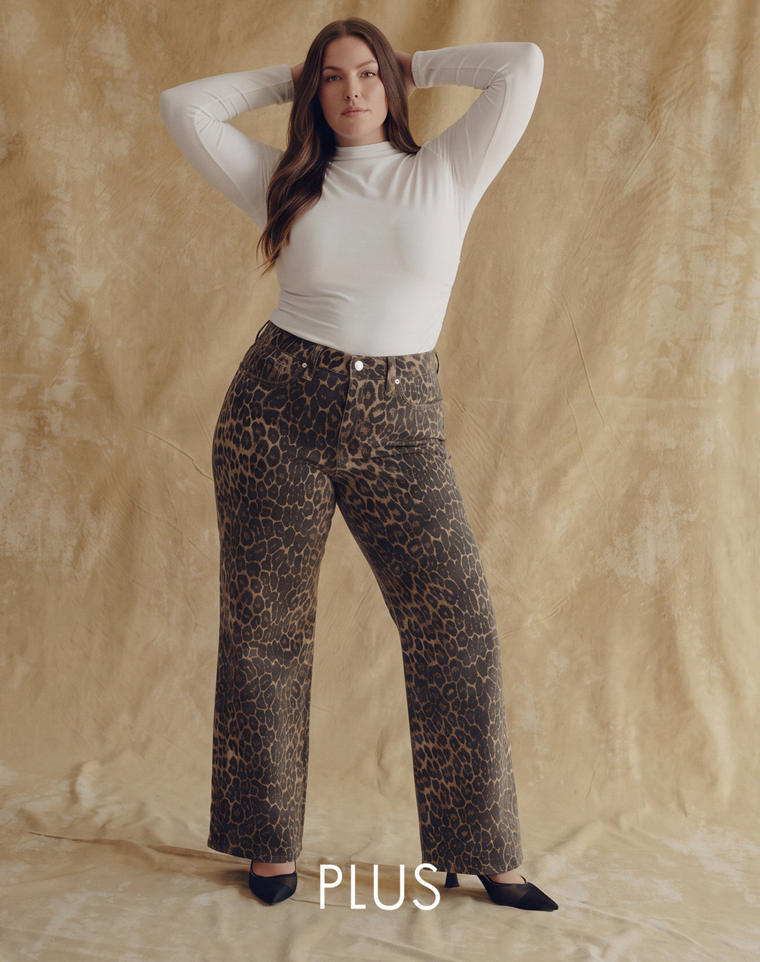 A Plus size model wearing a long sleeve white top and cheetah print pants. Text underneath model saying 'Plus'